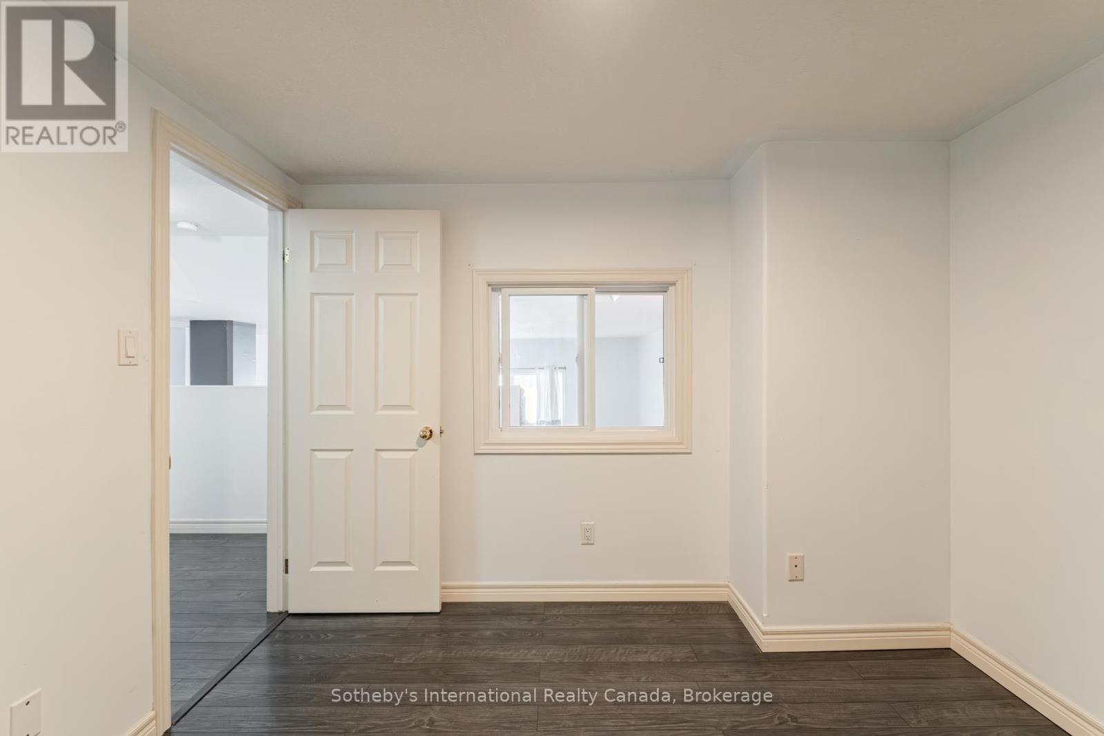 Empty room with dark wood flooring, a small window, and an open doorway.