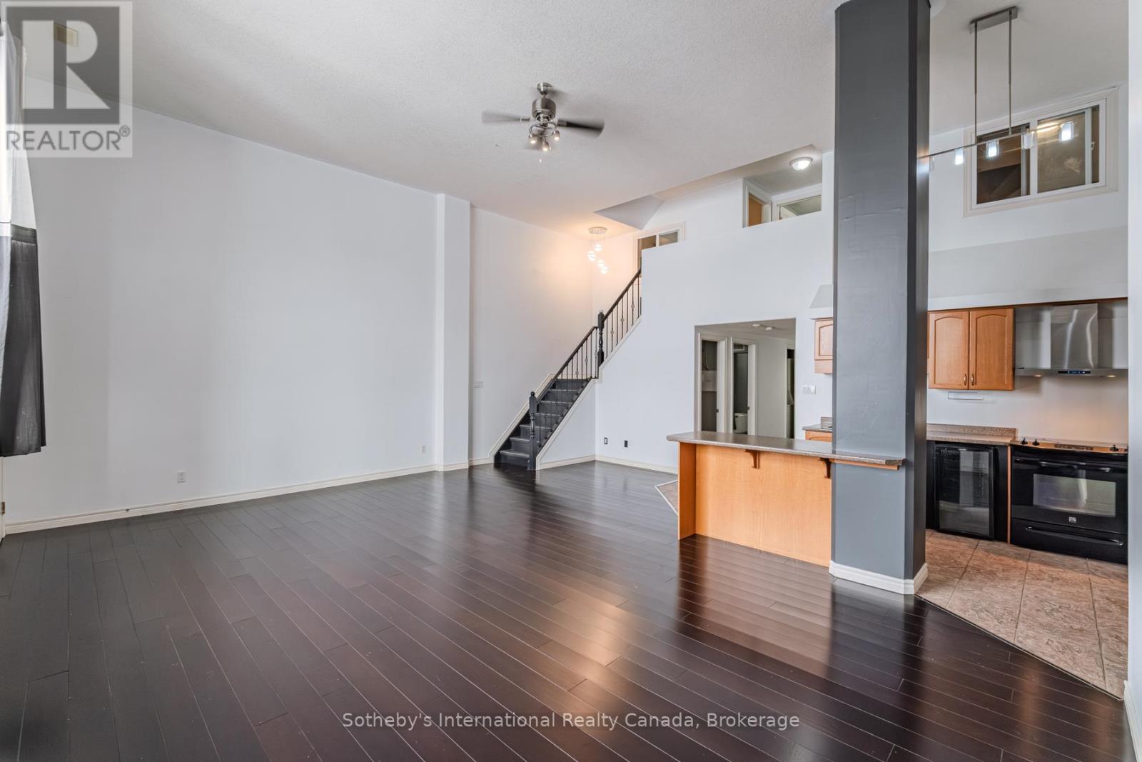 Open living room with dark hardwood floors, a staircase, and an adjoining kitchen.