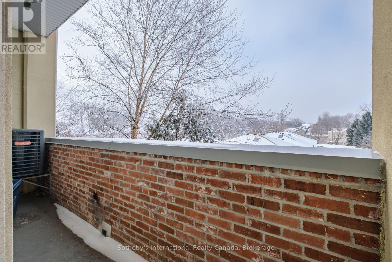 Balcony with a brick parapet overlooking snow-covered rooftops and leafless trees.