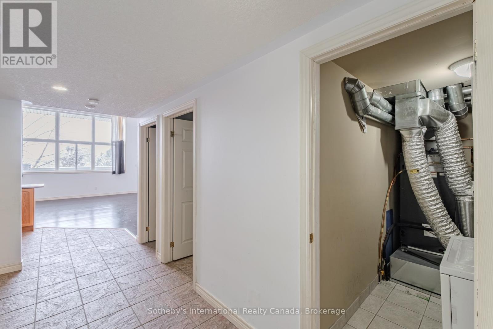 Utility room with exposed HVAC ductwork beside a tiled hallway and bright living area.