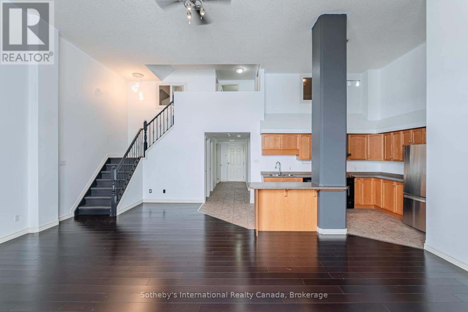 Open-plan kitchen and living area with dark floors, a staircase, and a breakfast bar.