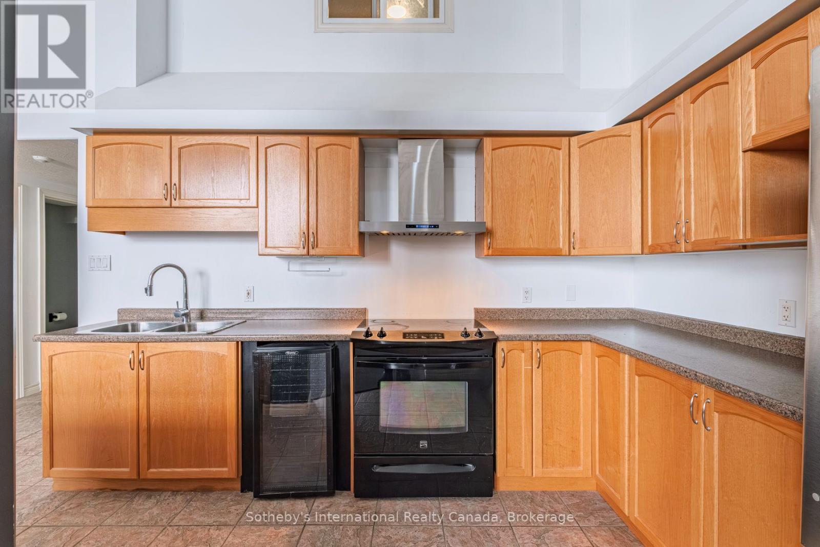 Kitchen with honey-colored wood cabinets, corner counters, black range, and built-in dishwasher.
