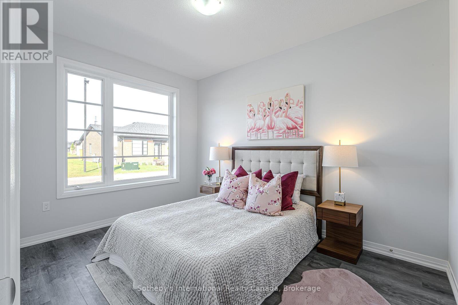 Staged bedroom with a tufted bed, pink flamingo artwork, and a large divided window.