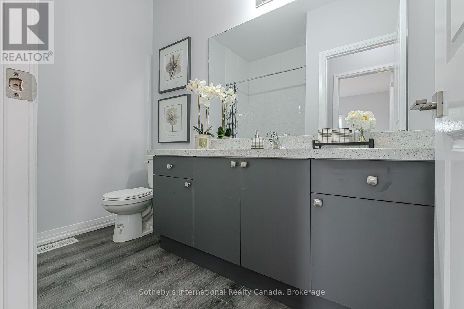 Bathroom with a wide gray vanity, speckled countertop, large mirror, and toilet.