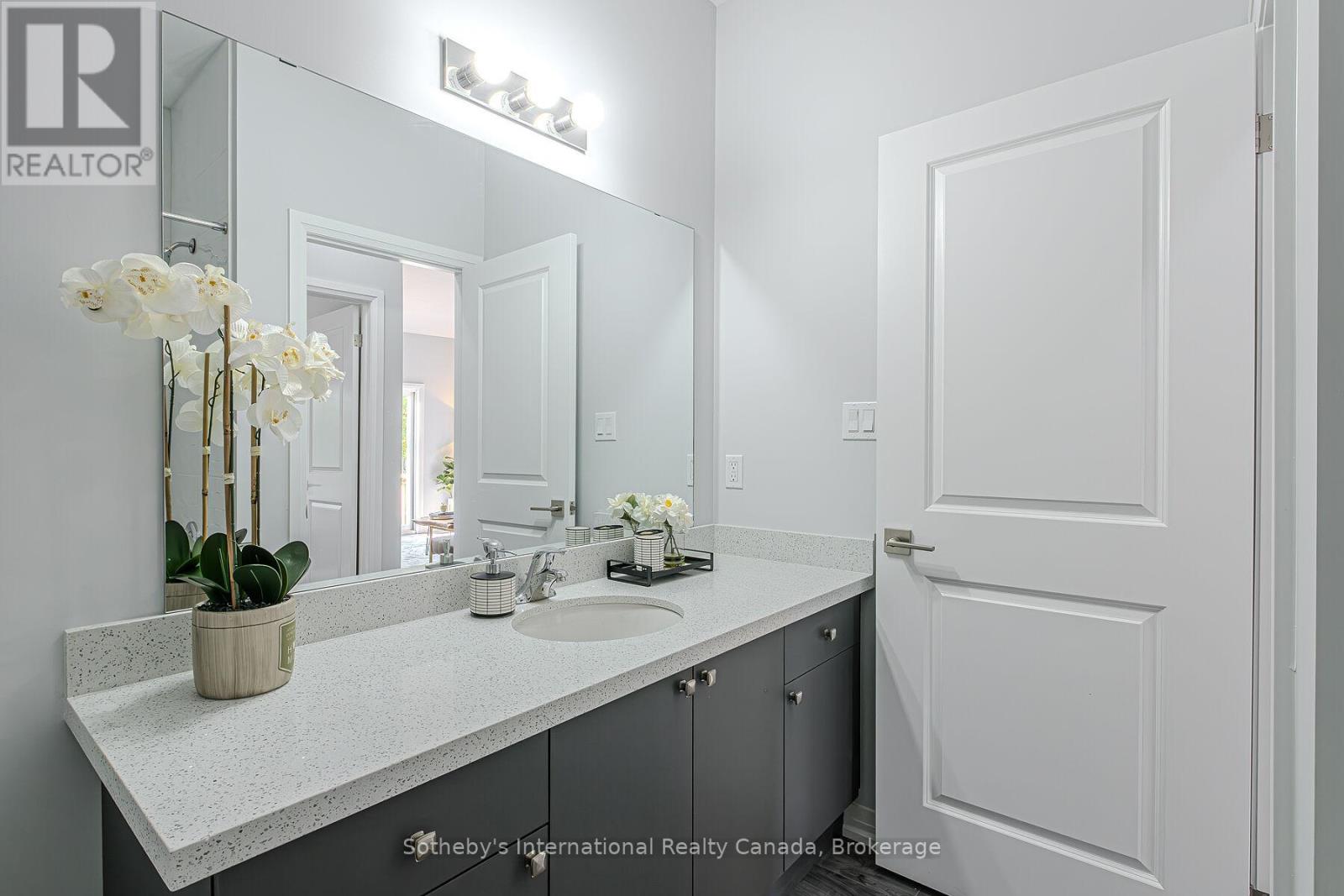 Bathroom vanity with speckled countertop, dark cabinetry, and an orchid beside a mirrored wall.