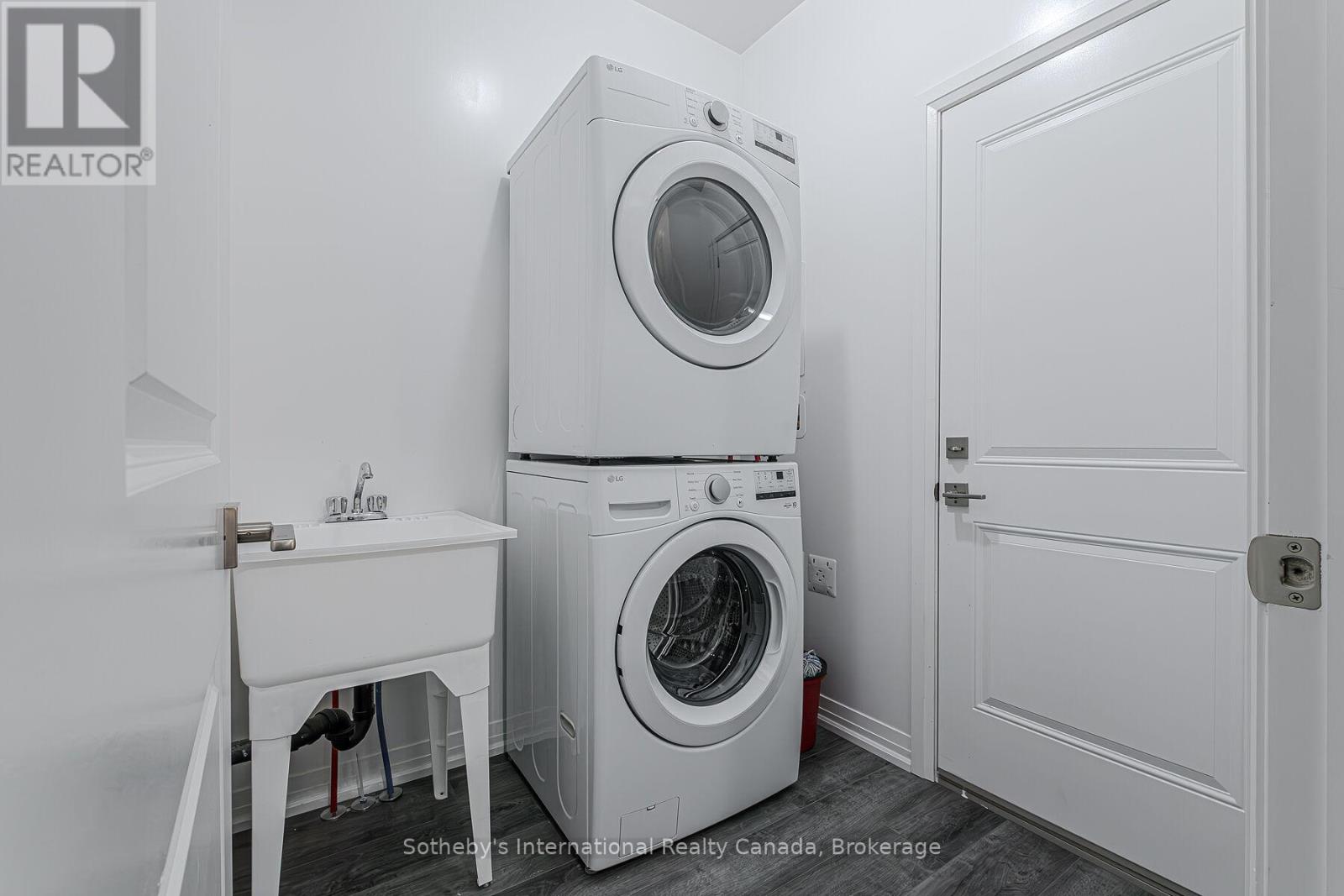 Laundry room with stacked front-loading washer and dryer beside a utility sink.