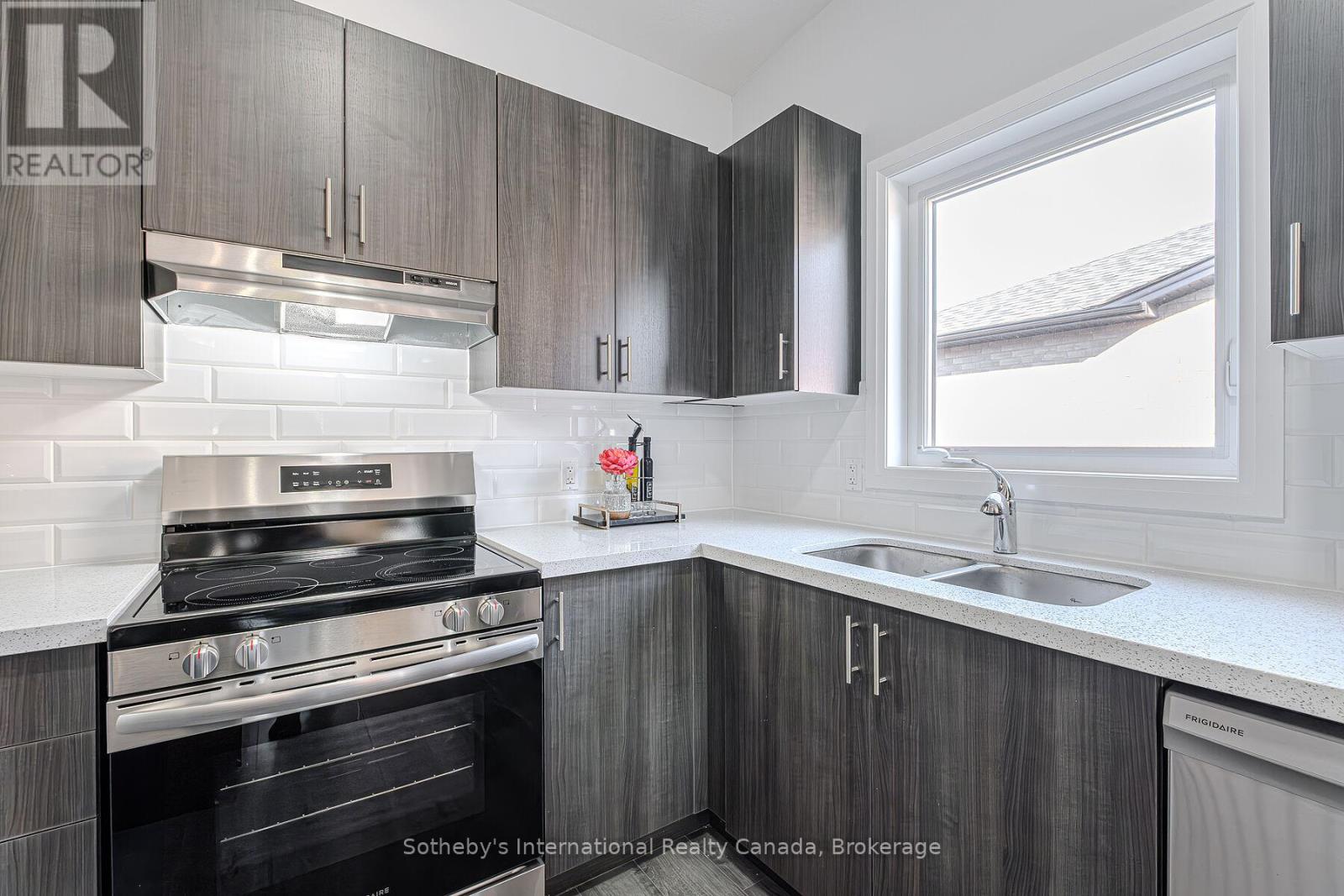 Kitchen with dark wood cabinetry, stainless steel range, and a double-basin sink beneath a window.