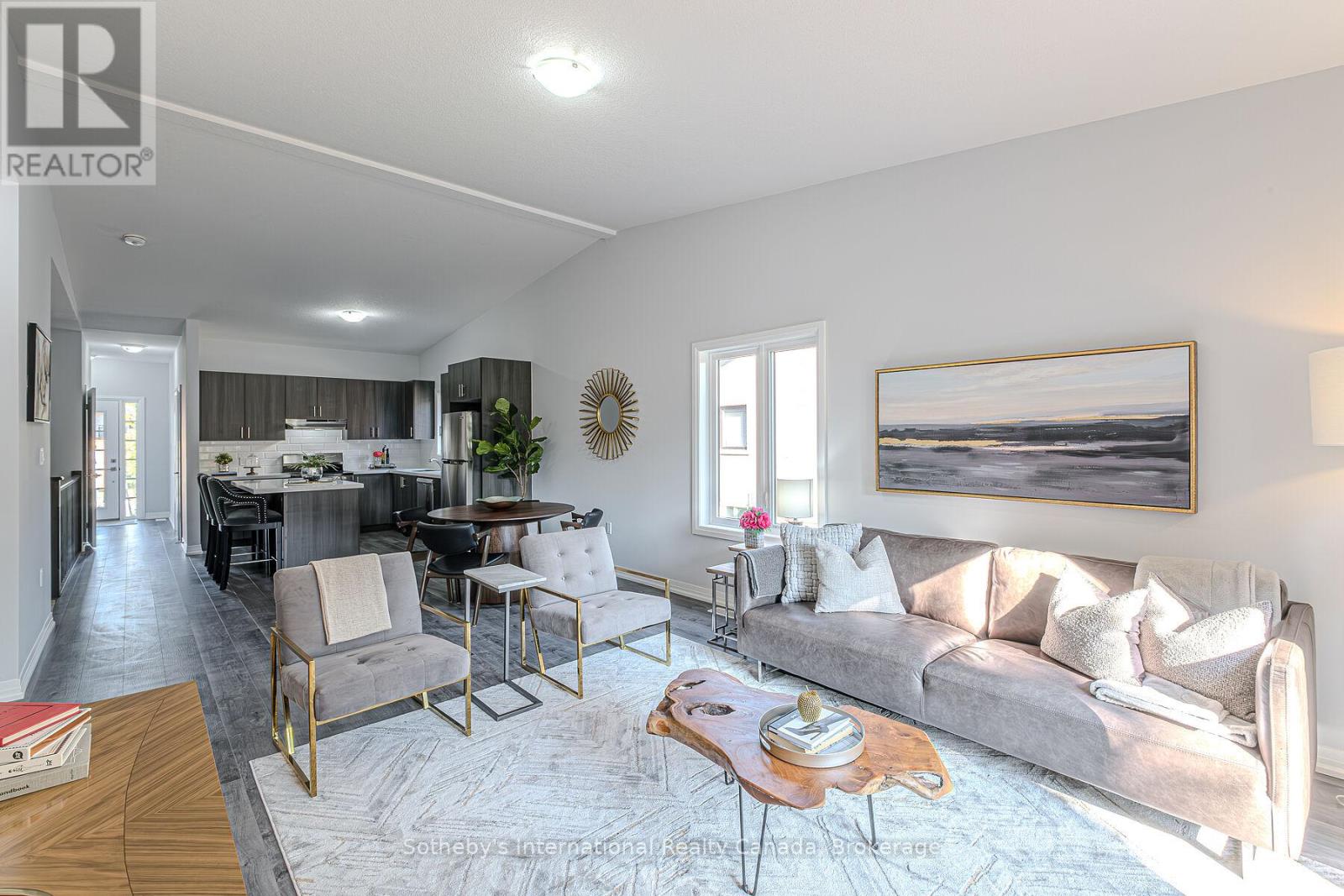 Staged open-plan living room and kitchen with gray seating, dark cabinetry, and a wood coffee table.