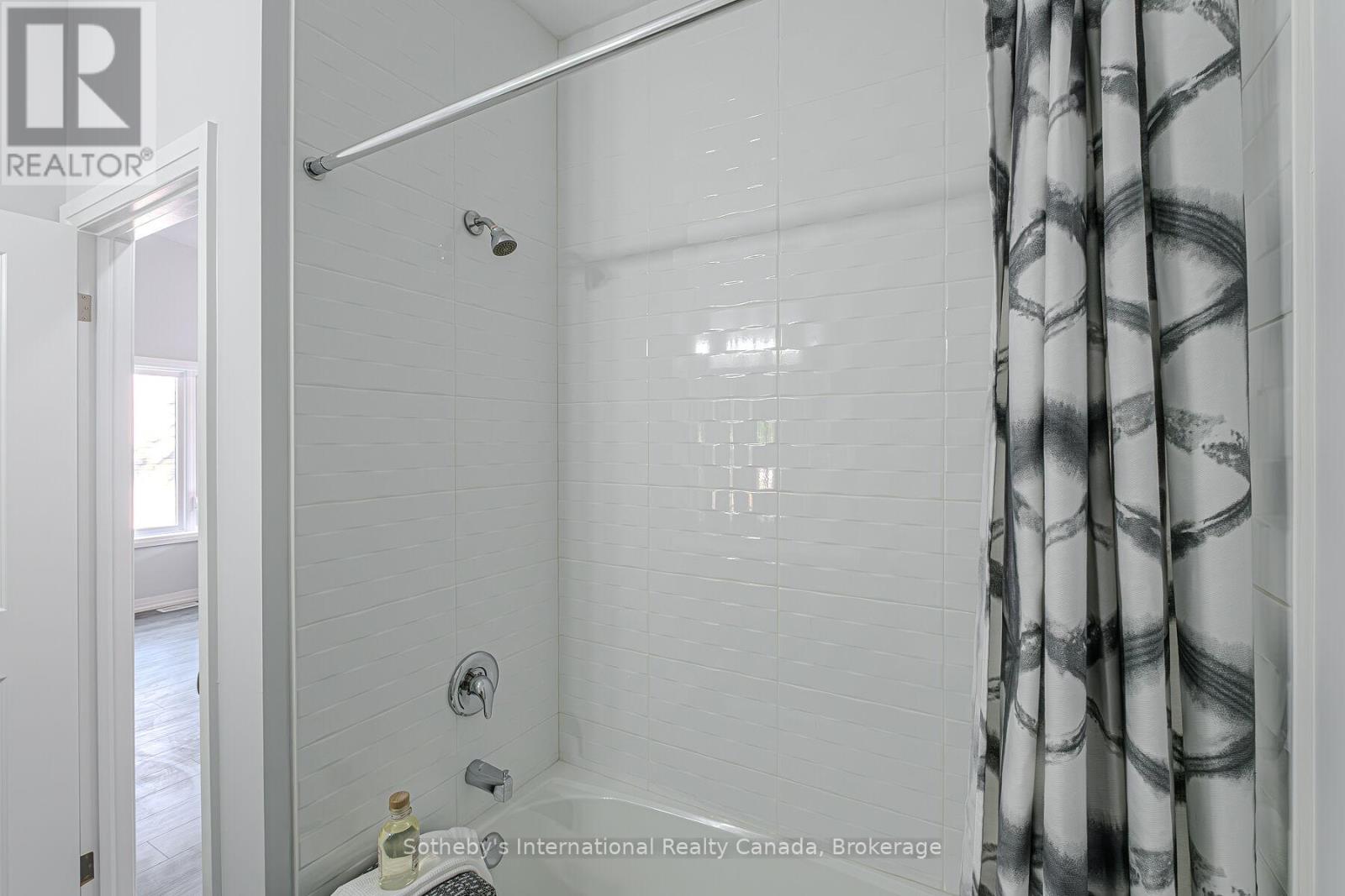 Bathroom with a white tiled tub and shower, chrome fixtures, and a black-and-white patterned curtain.