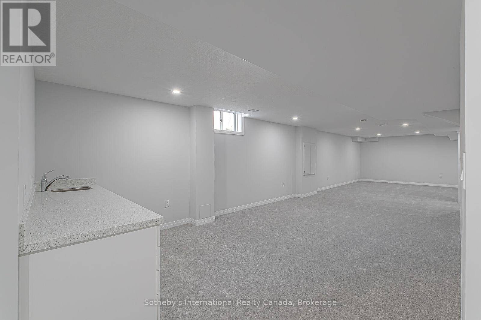 Empty carpeted basement recreation room with a small sink counter and recessed lighting.