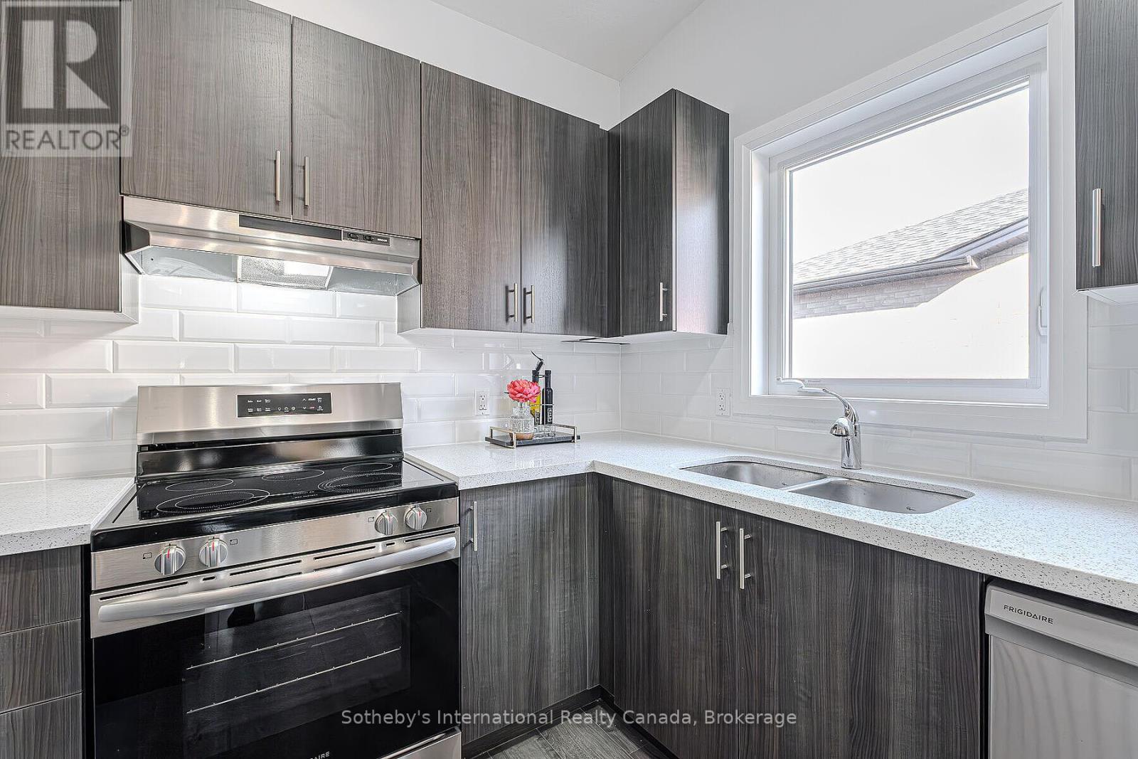 Kitchen with dark wood cabinets, stainless steel appliances, white tile backsplash, and a window over the sink.