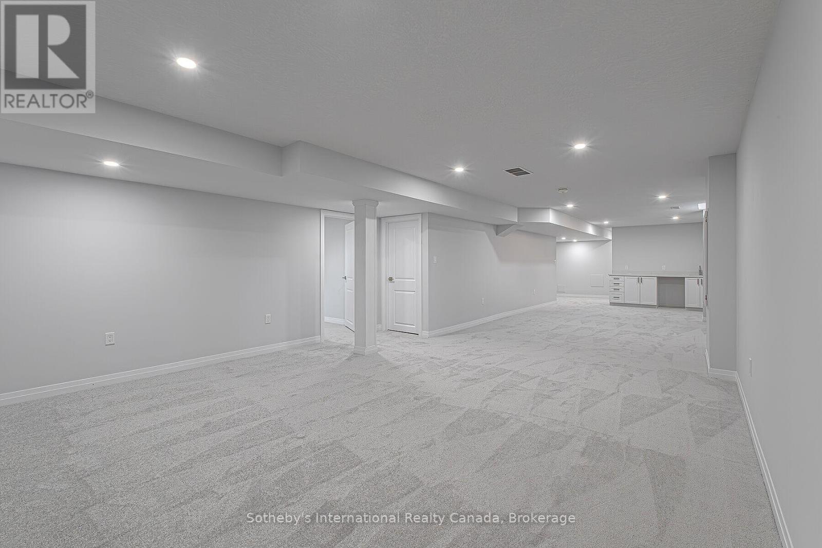 Finished basement with gray carpet, recessed lighting, and a kitchenette at the far end.