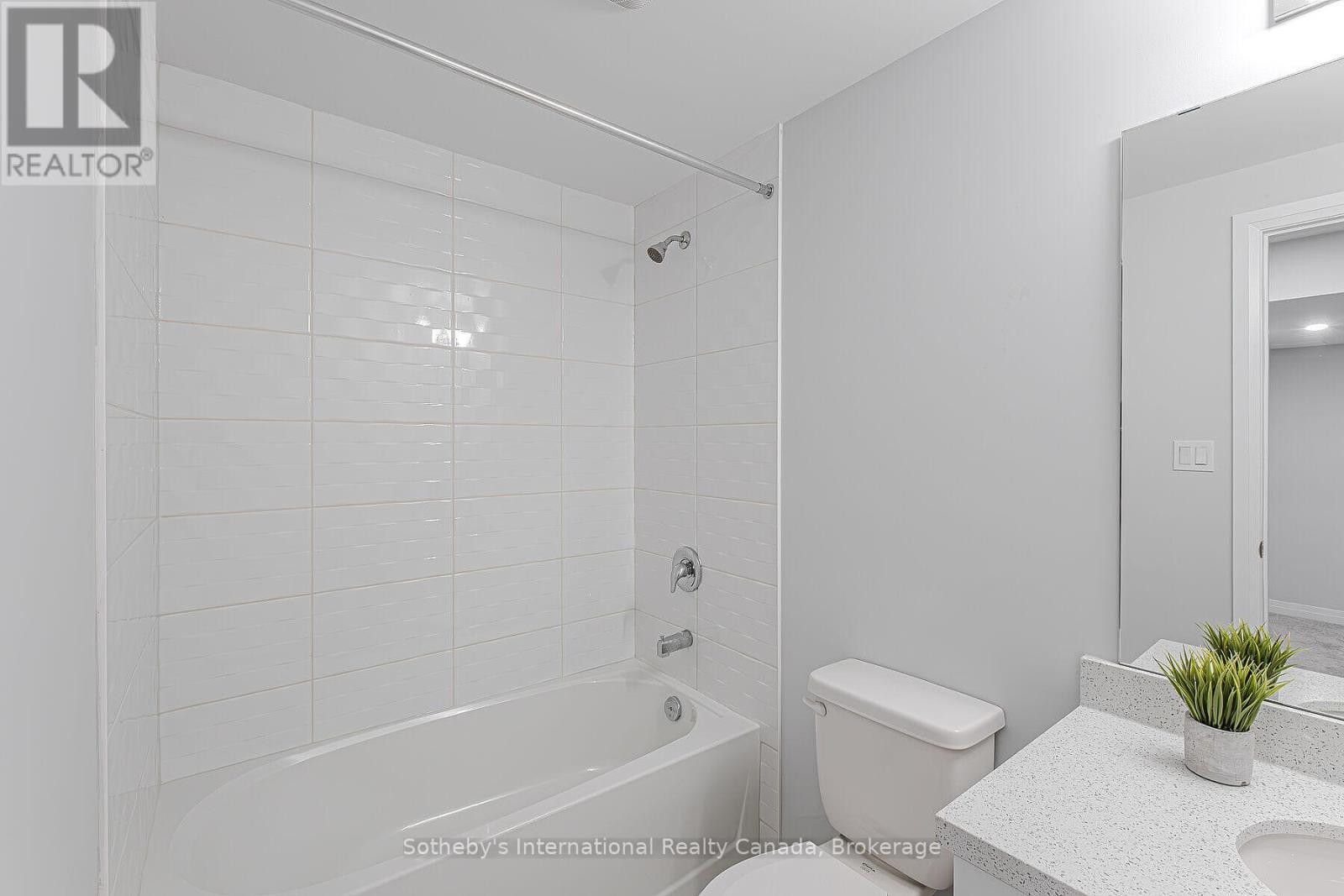 Bathroom with a white tiled tub-shower, toilet, and speckled vanity with a small plant.