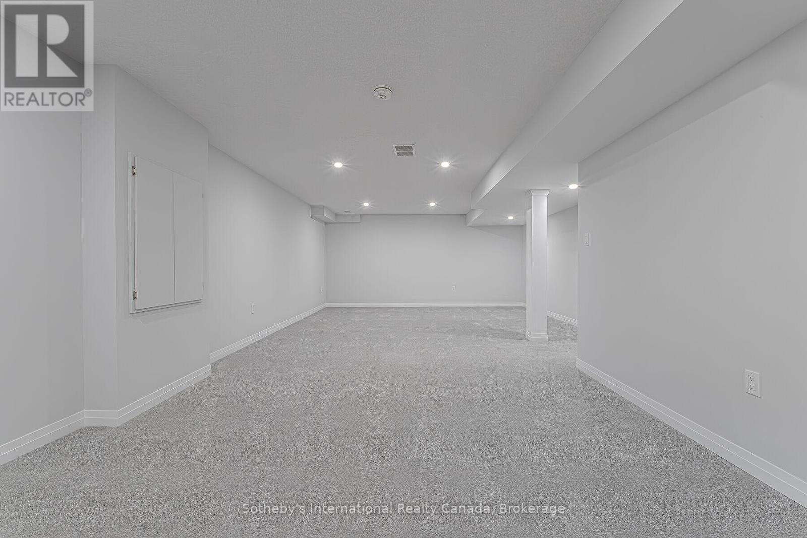Finished basement with gray carpeting, recessed lights, and a support column.
