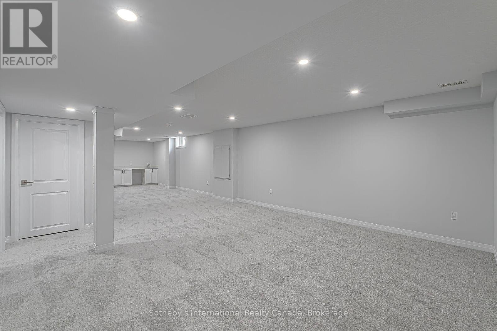 Unfurnished basement recreation room with gray carpet, recessed lights, and a small kitchenette.