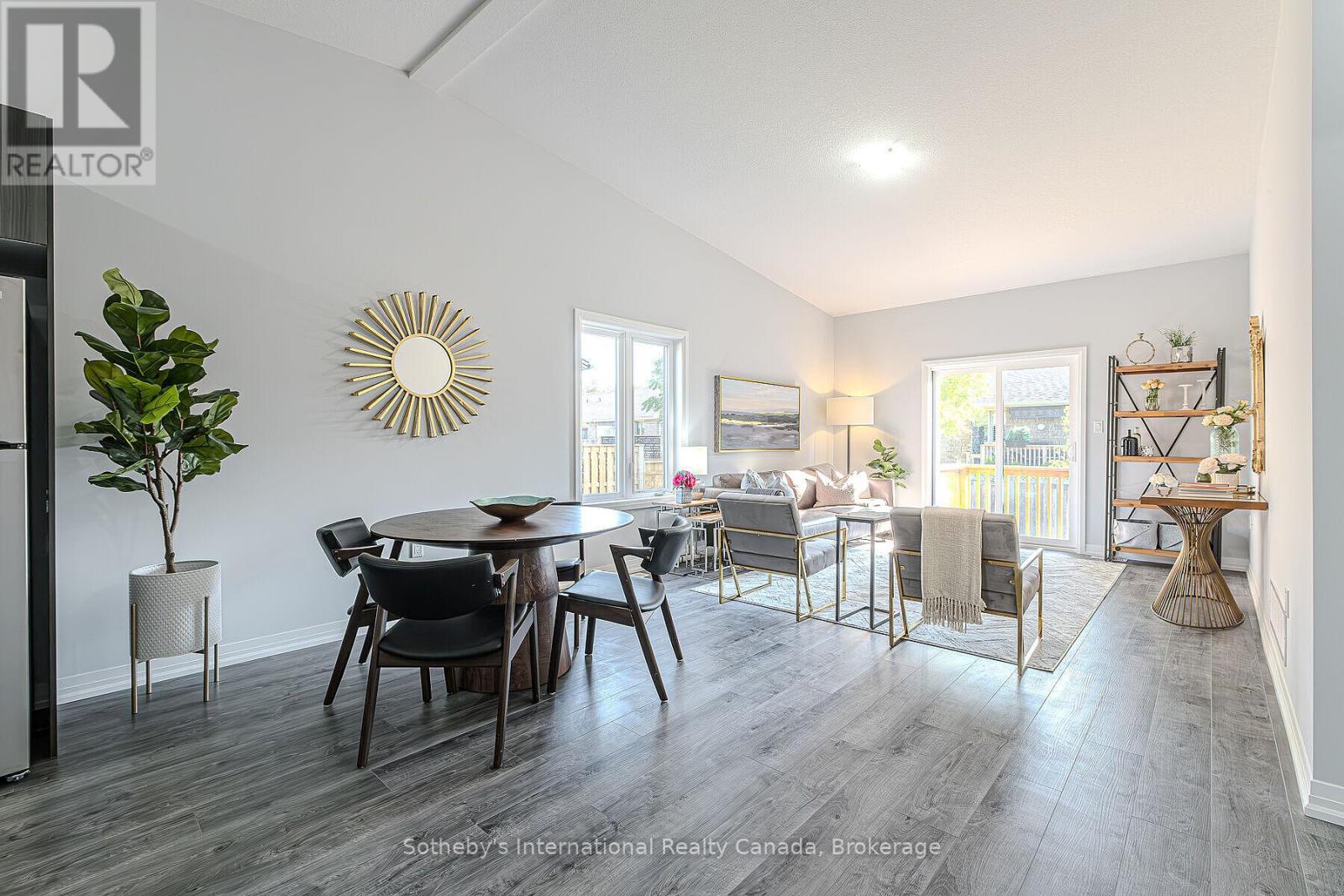 Staged open-concept dining and living room with gray floors and sliding doors to a deck.
