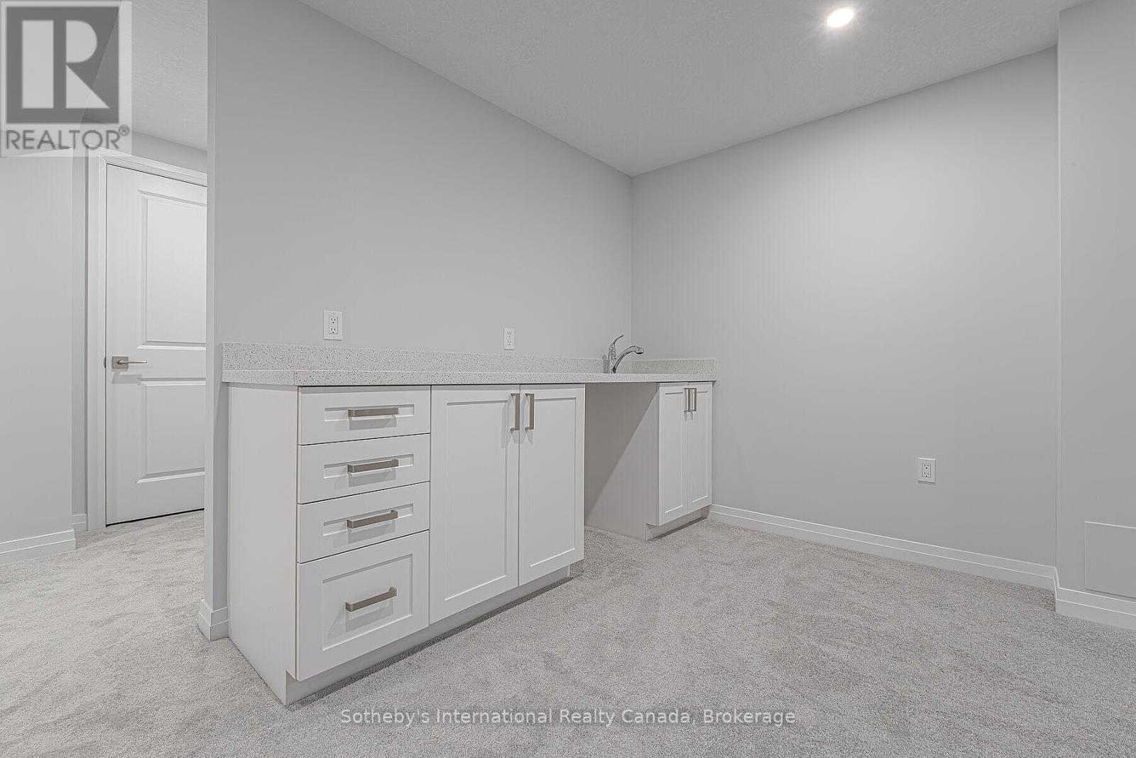 Carpeted room with white built-in cabinets, a countertop, and sink.