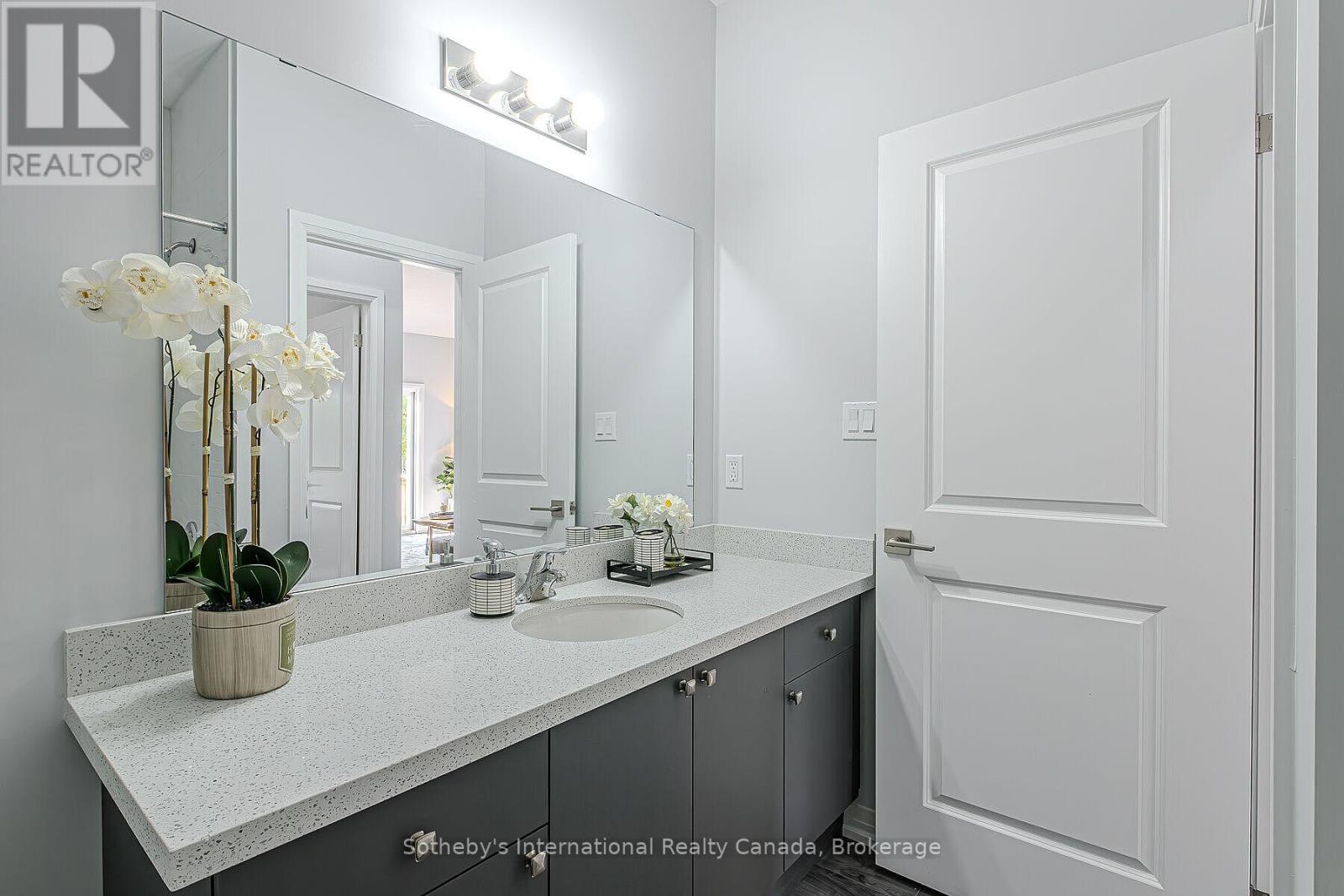 Bathroom vanity with a speckled countertop, dark cabinetry, large mirror, and white orchid.
