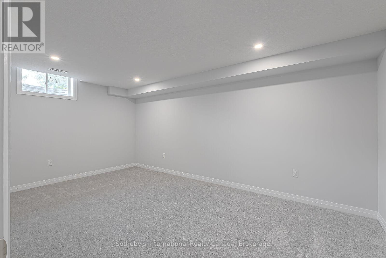 Empty basement room with gray carpeting, recessed lights, and small high-set windows.