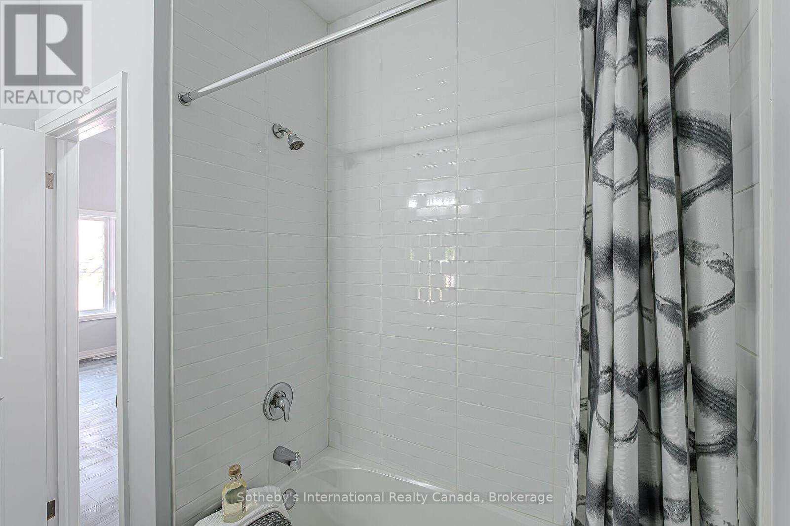 Bathroom shower with white subway tile, chrome fixtures, and a black-and-white patterned curtain.
