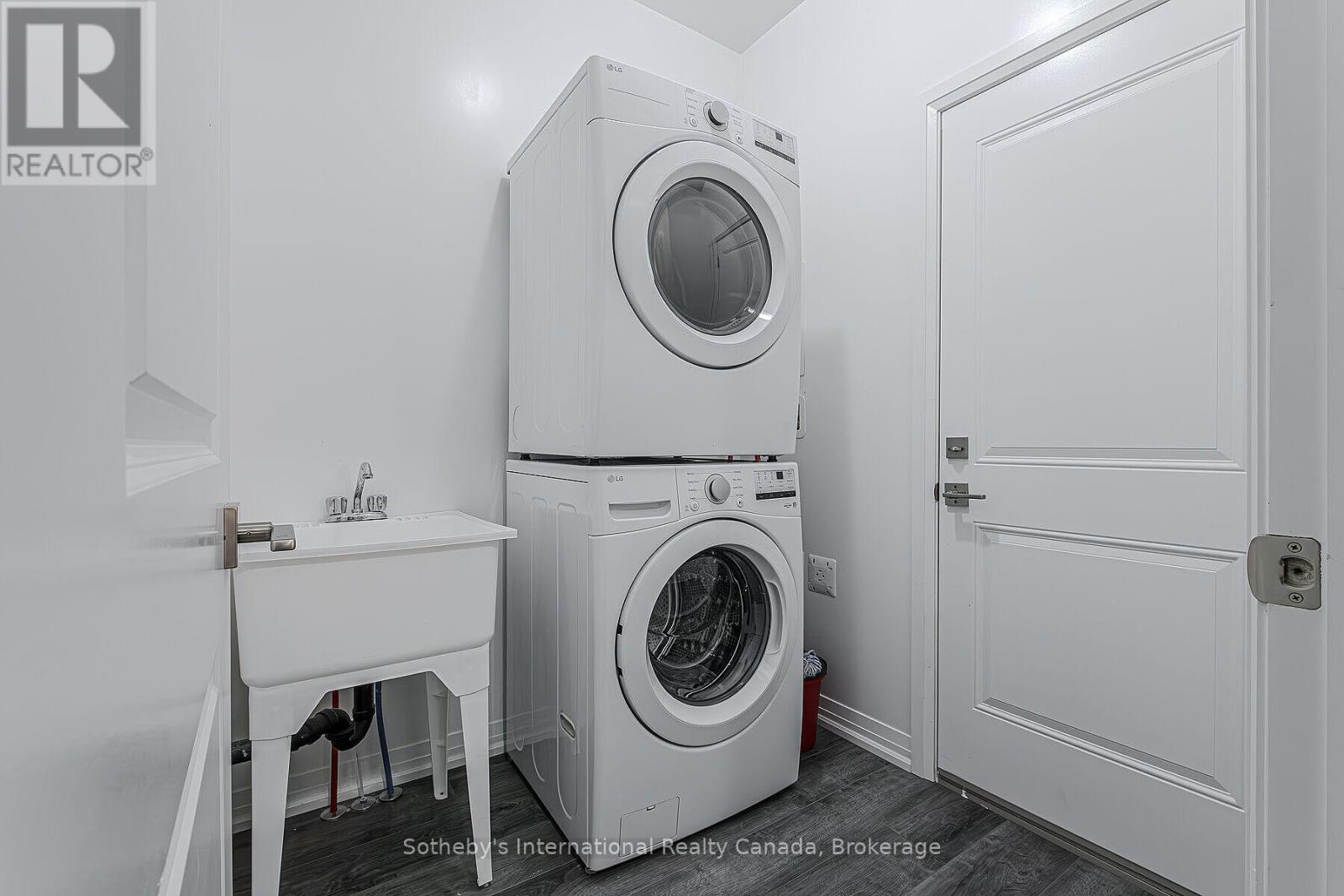 Laundry room with stacked front-load washer and dryer beside a utility sink.