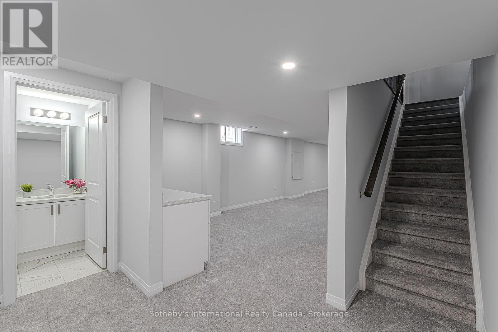 Basement recreation area with gray carpet, a staircase, and an adjoining bathroom.