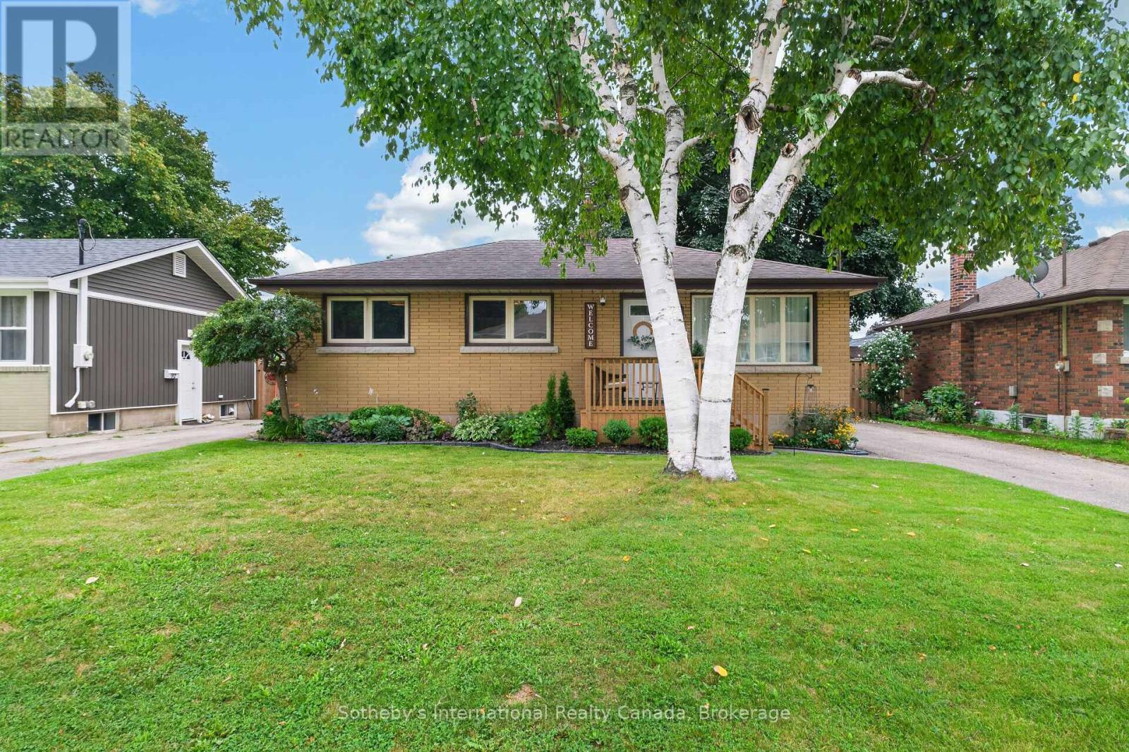 Single-storey brick house with a wooden porch, mature birch tree, and broad front lawn.