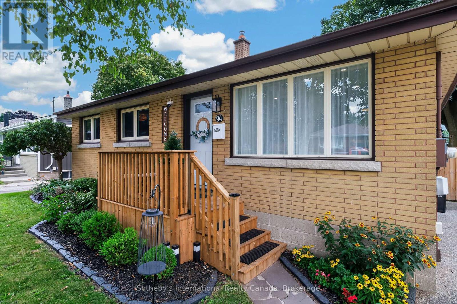 Single-story brick home with a wooden porch, front steps, and flower beds.