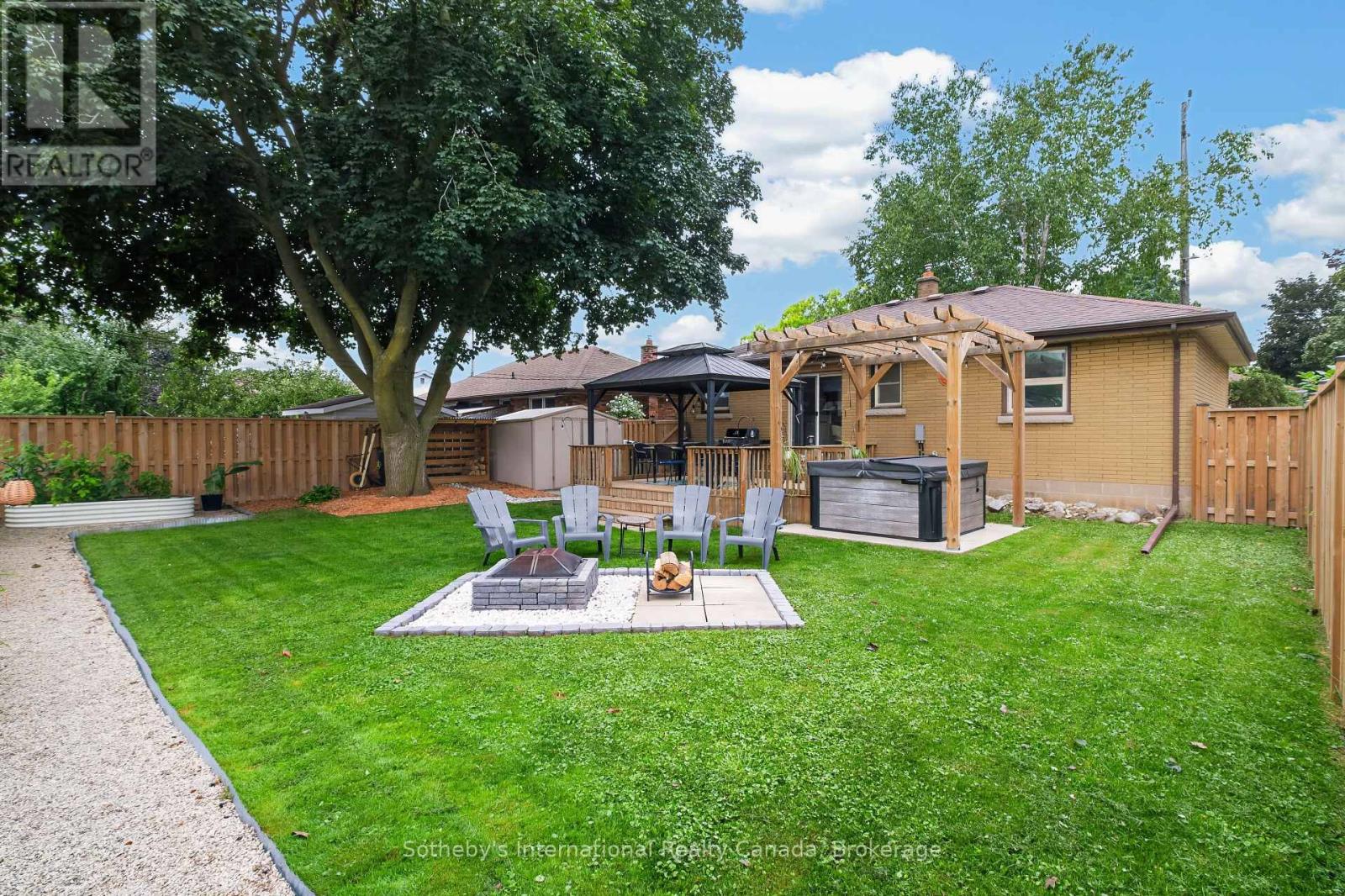 Backyard with a pergola-covered patio, hot tub, fire pit, and fenced lawn.