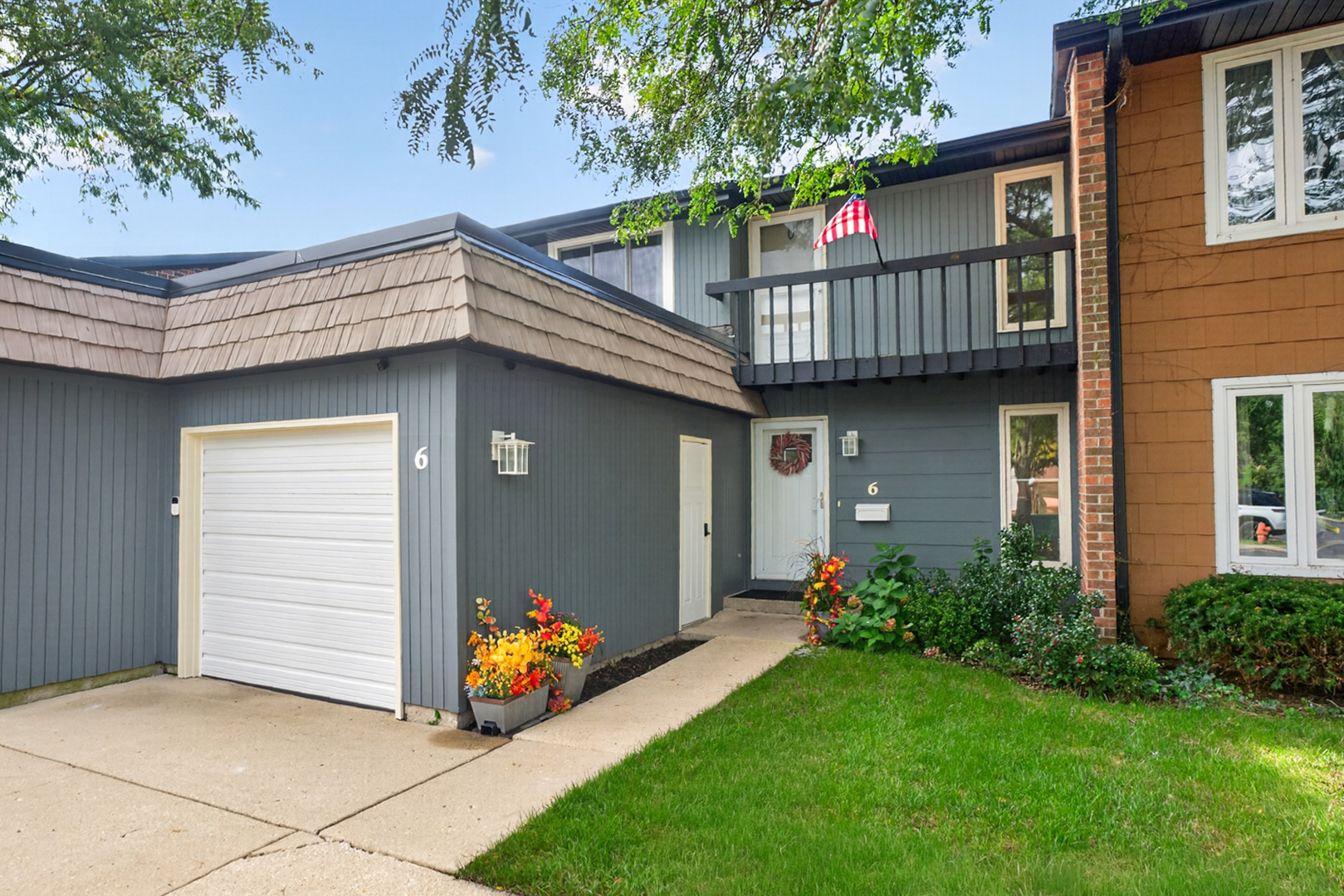 Gray home exterior with a raised balcony, white garage door, and flower-lined entry.