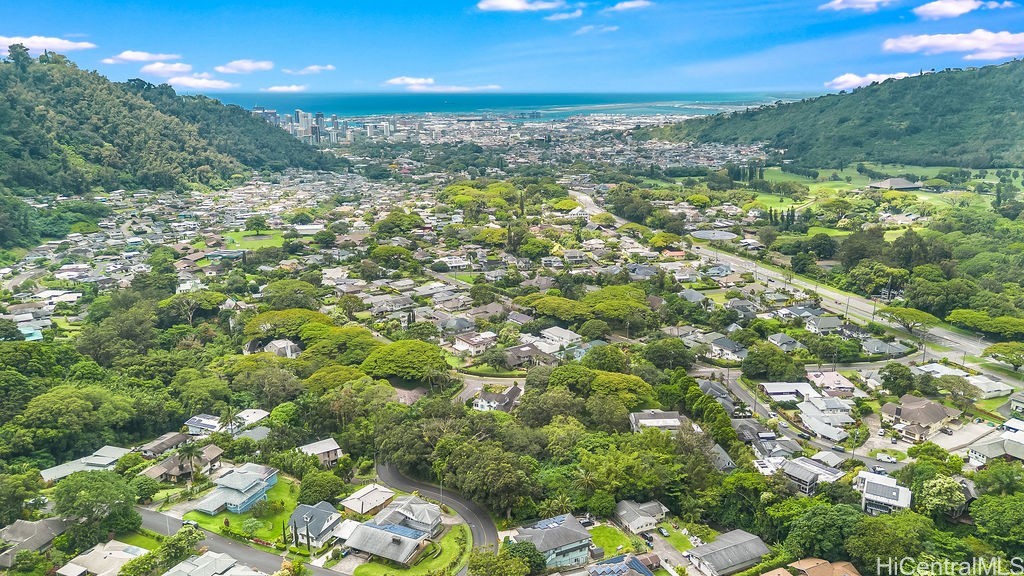 Aerial view of a Honolulu neighborhood between green hills, with the city and ocean in the distance.