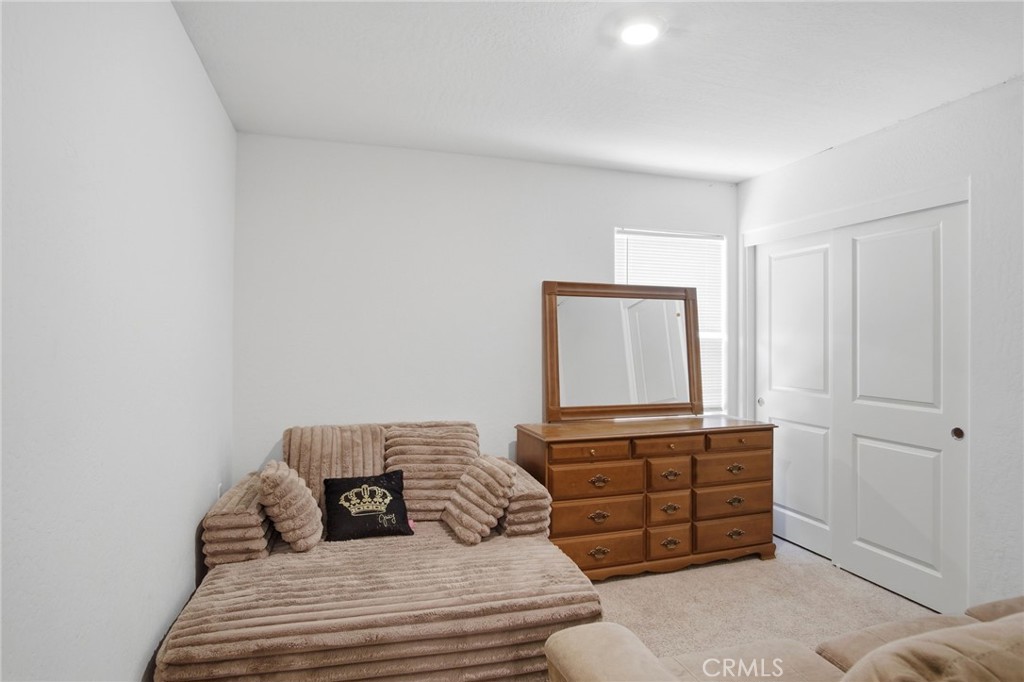 Bedroom with a beige daybed, wooden dresser and mirror, and white closet doors.