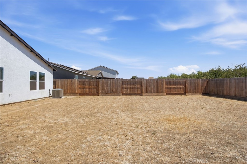 Dry backyard with a wooden privacy fence and the side of the house.