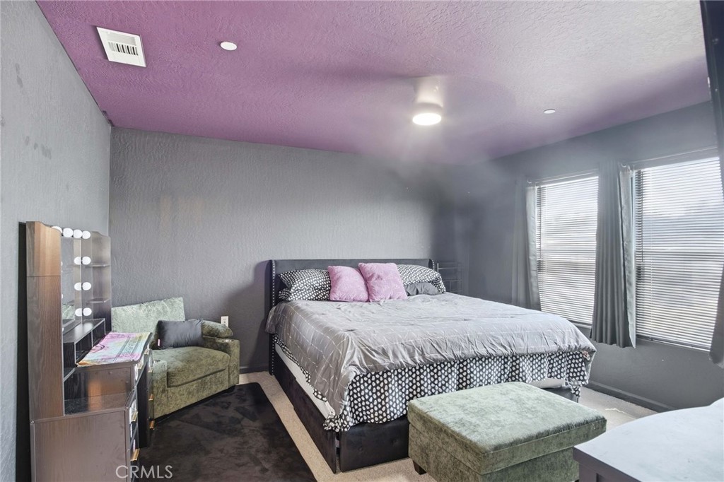 Bedroom with a large bed, purple ceiling, and green upholstered seating beside two windows.