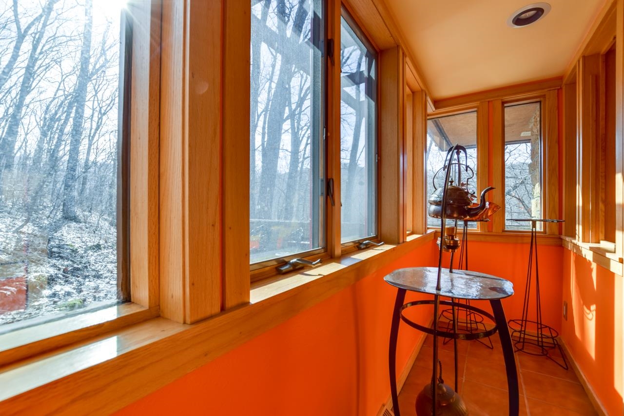 Sunroom with orange walls, wood-trimmed windows, and a small table overlooking snowy trees.