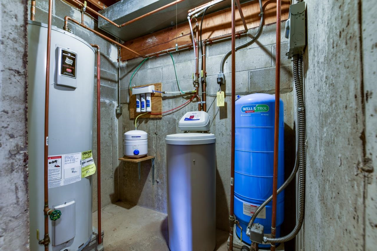 Basement utility room with water heater, filtration equipment, and a blue pressure tank.