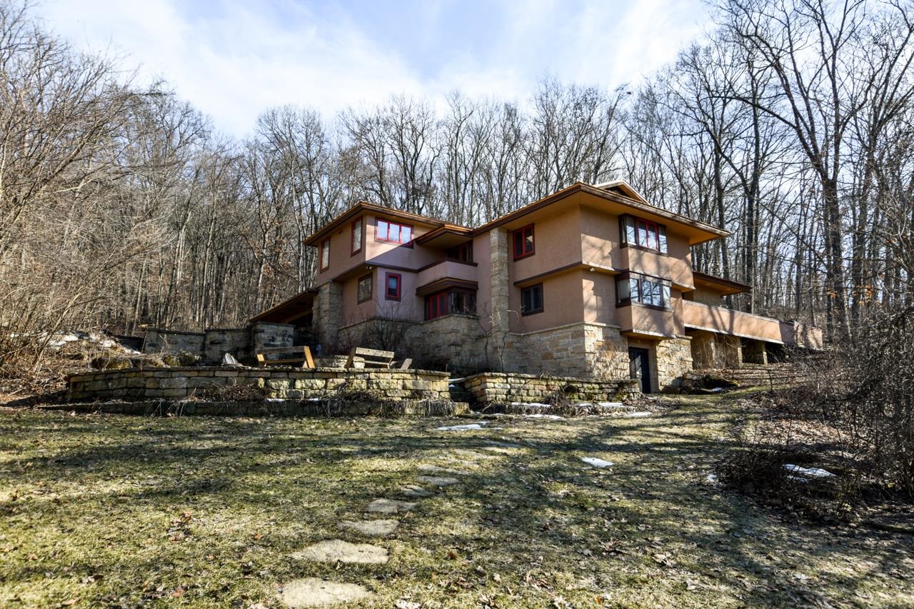 Multilevel tan stucco and stone home with a terraced patio among leafless trees.