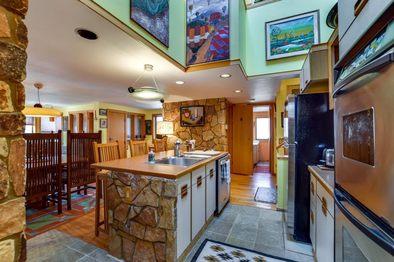 Kitchen with a stone-faced island, wood countertop, and dining area beneath a raised ceiling with artwork.