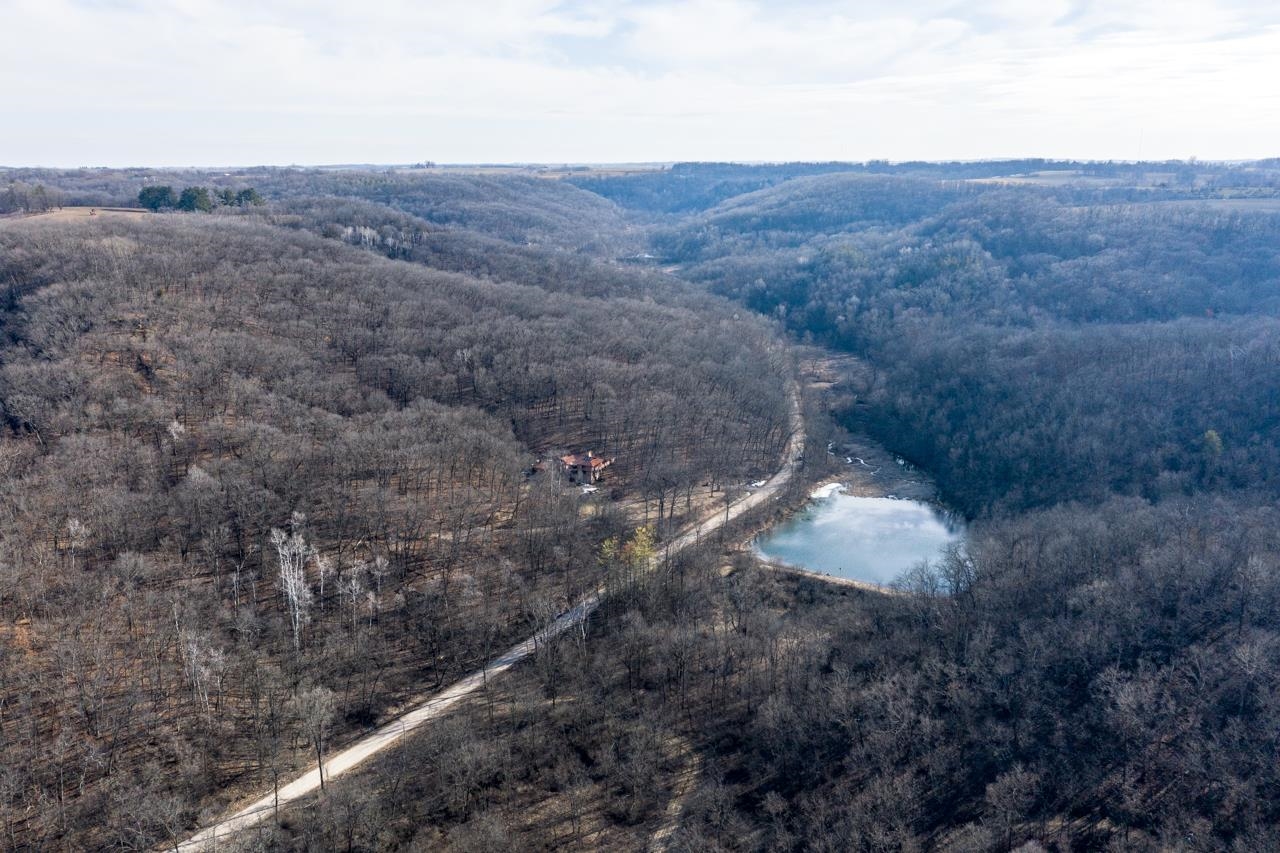 Aerial view of a wooded property with a house, winding driveway, and frozen pond.