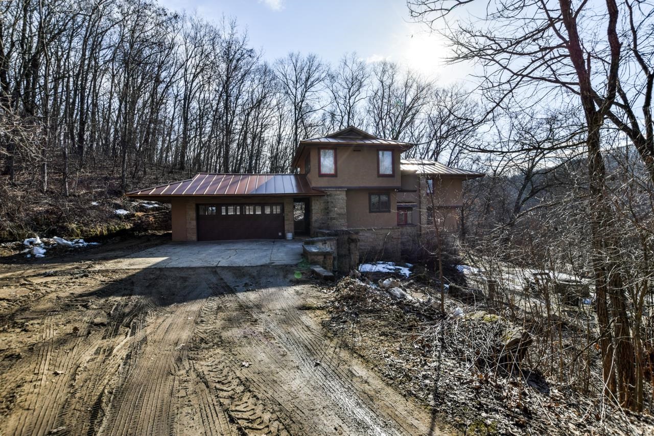 Brown two-story home with a metal roof and attached garage, surrounded by leafless woods.