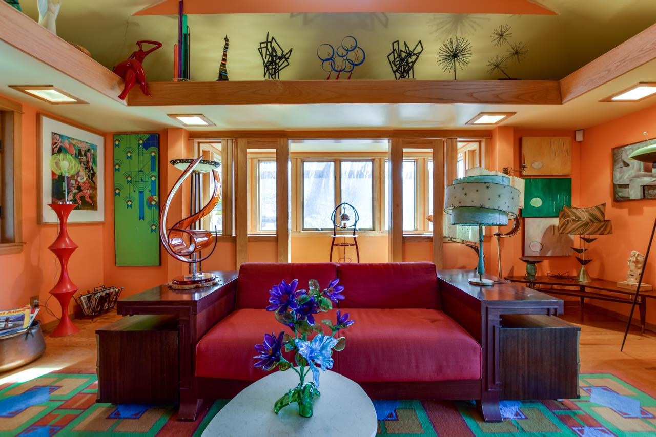 Living room with orange walls, a red sofa, and colorful geometric rug beneath a high display shelf.