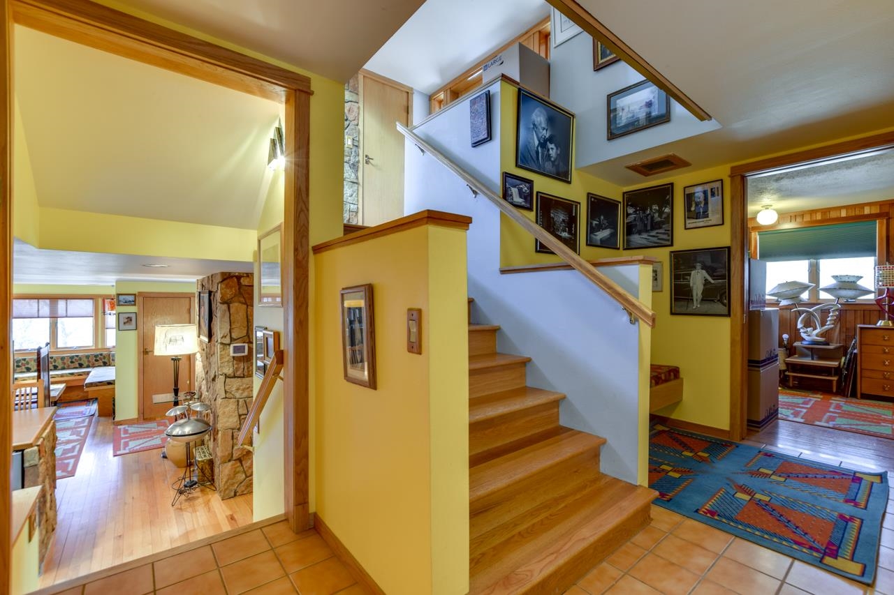 Home entryway with a wood staircase, framed photographs, and tiled floor.