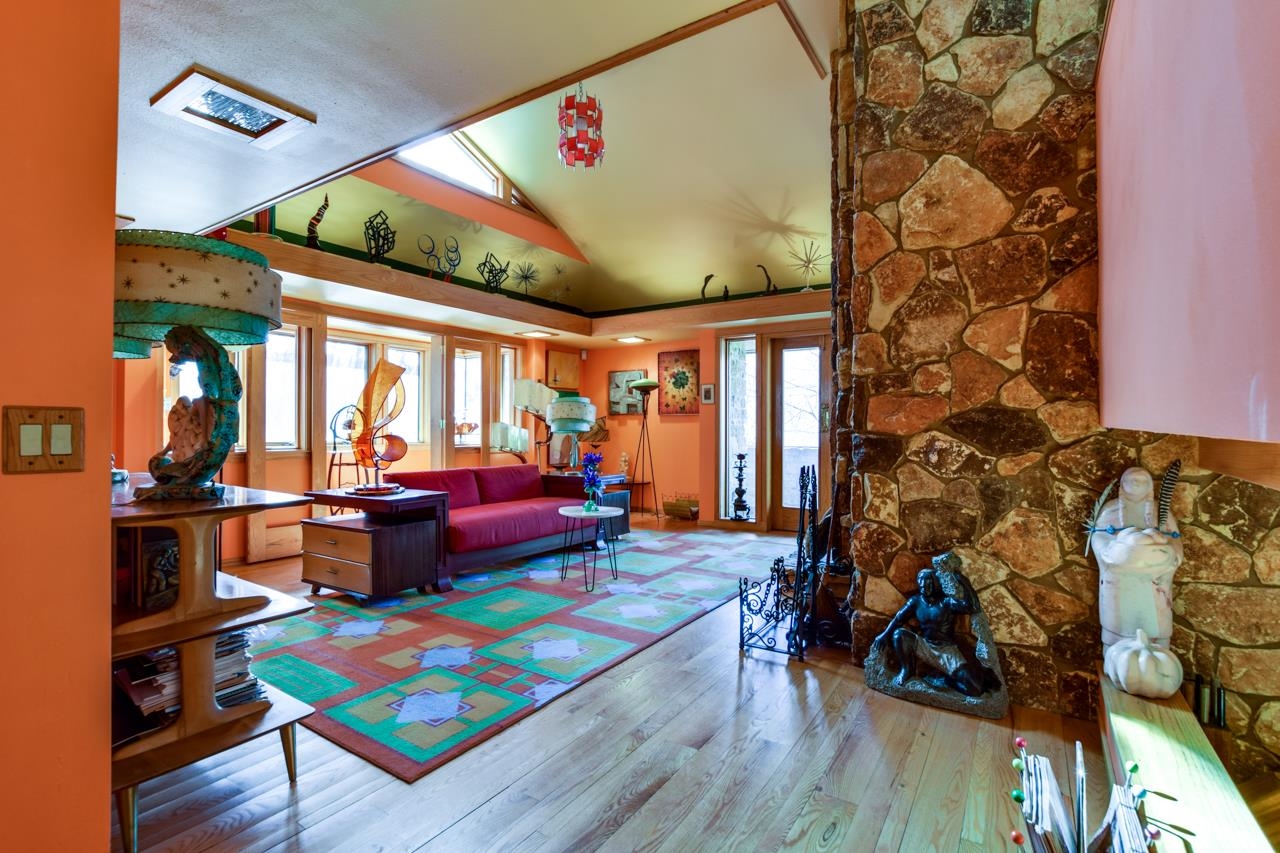 Living room with a vaulted ceiling, floor-to-ceiling stone fireplace, and colorful geometric rug.