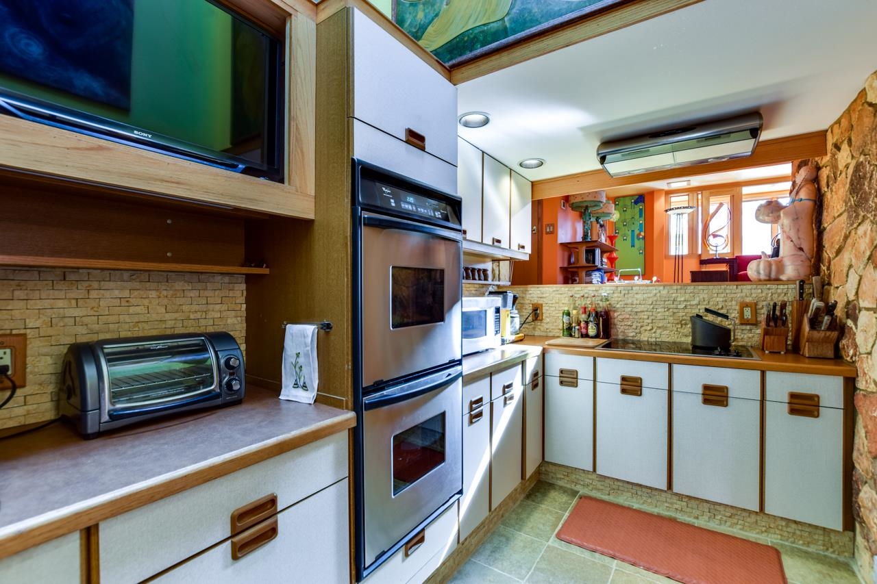 Kitchen with built-in double oven, stone backsplash, and wood-trimmed white cabinets.