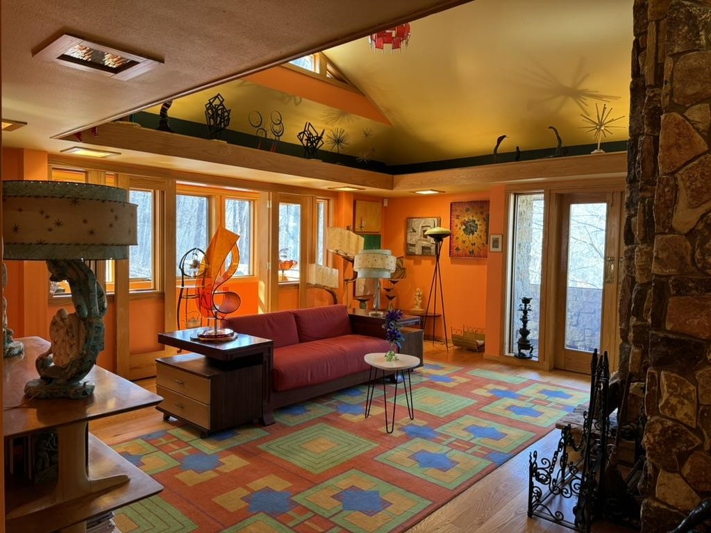 Living room with orange walls, red sofa, colorful geometric rug, and stone fireplace.