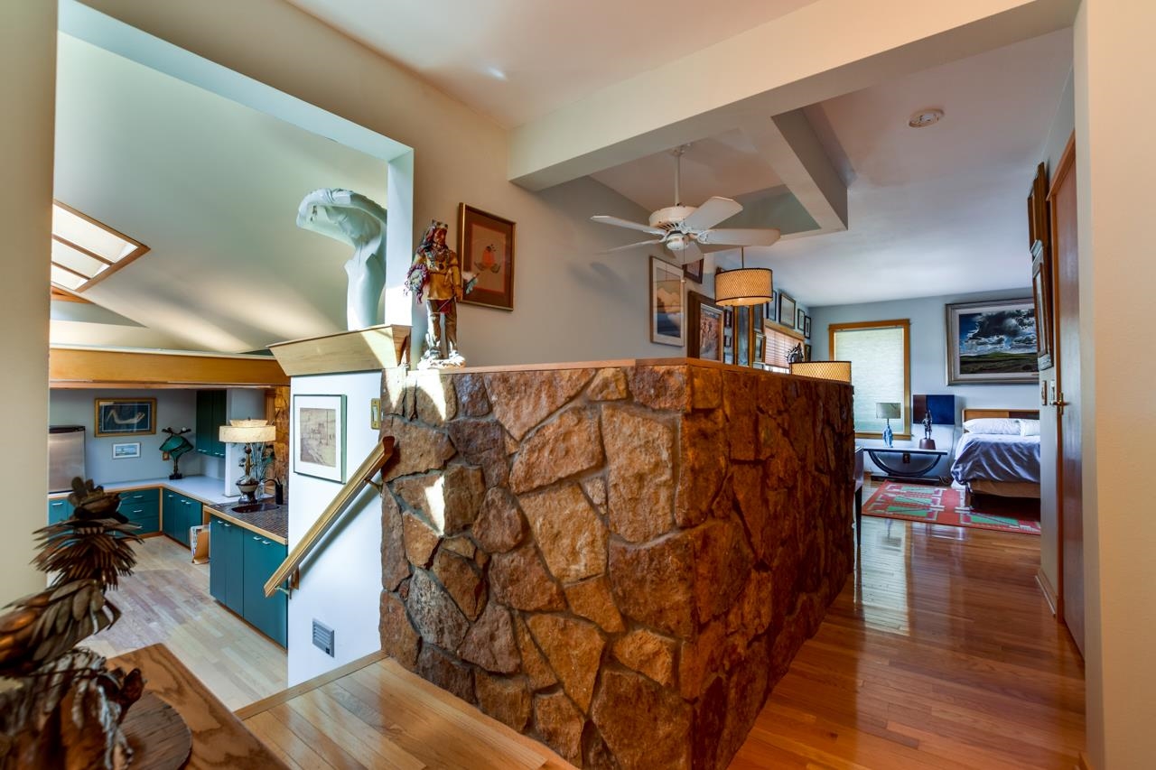 Home interior with a stone half wall dividing a teal-cabinet kitchen from a bedroom.