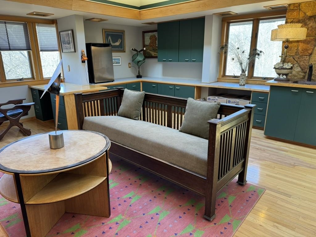 Furnished sitting area with a wood daybed, round table, colorful rug, and teal built-in cabinets.