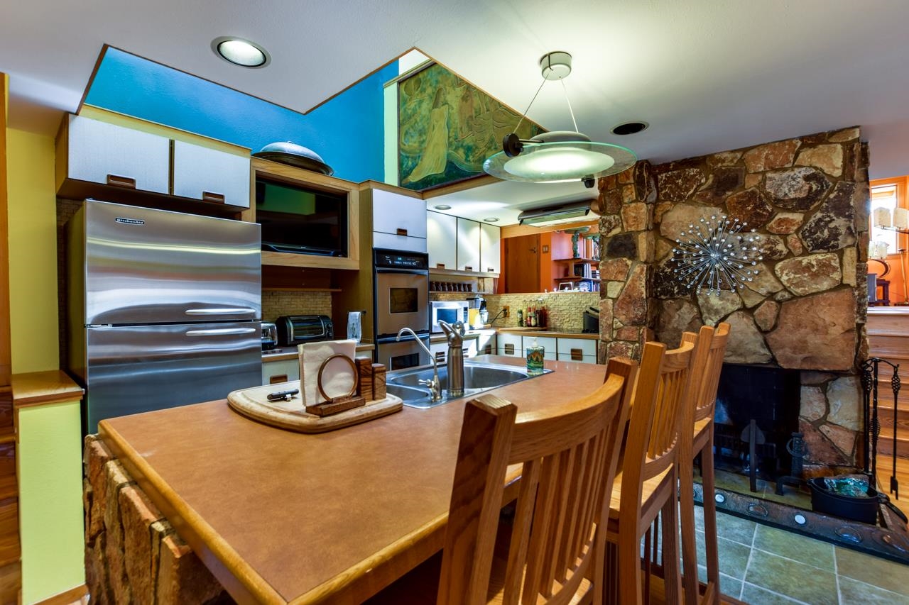 Kitchen with a large brown island, wooden bar stools, stainless steel appliances, and a stone fireplace.