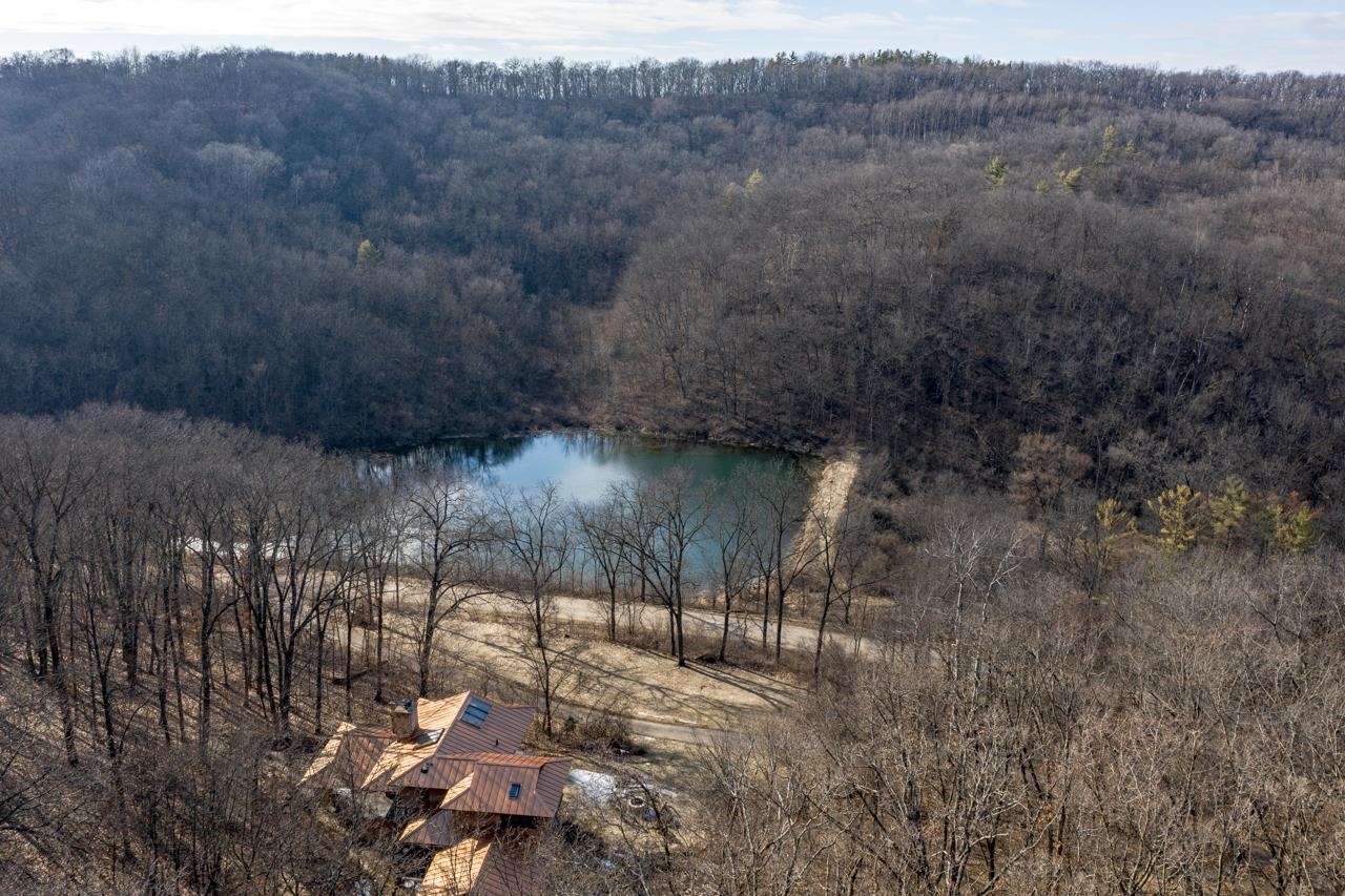 Aerial view of a wooded property with a pond behind a house and leafless trees.