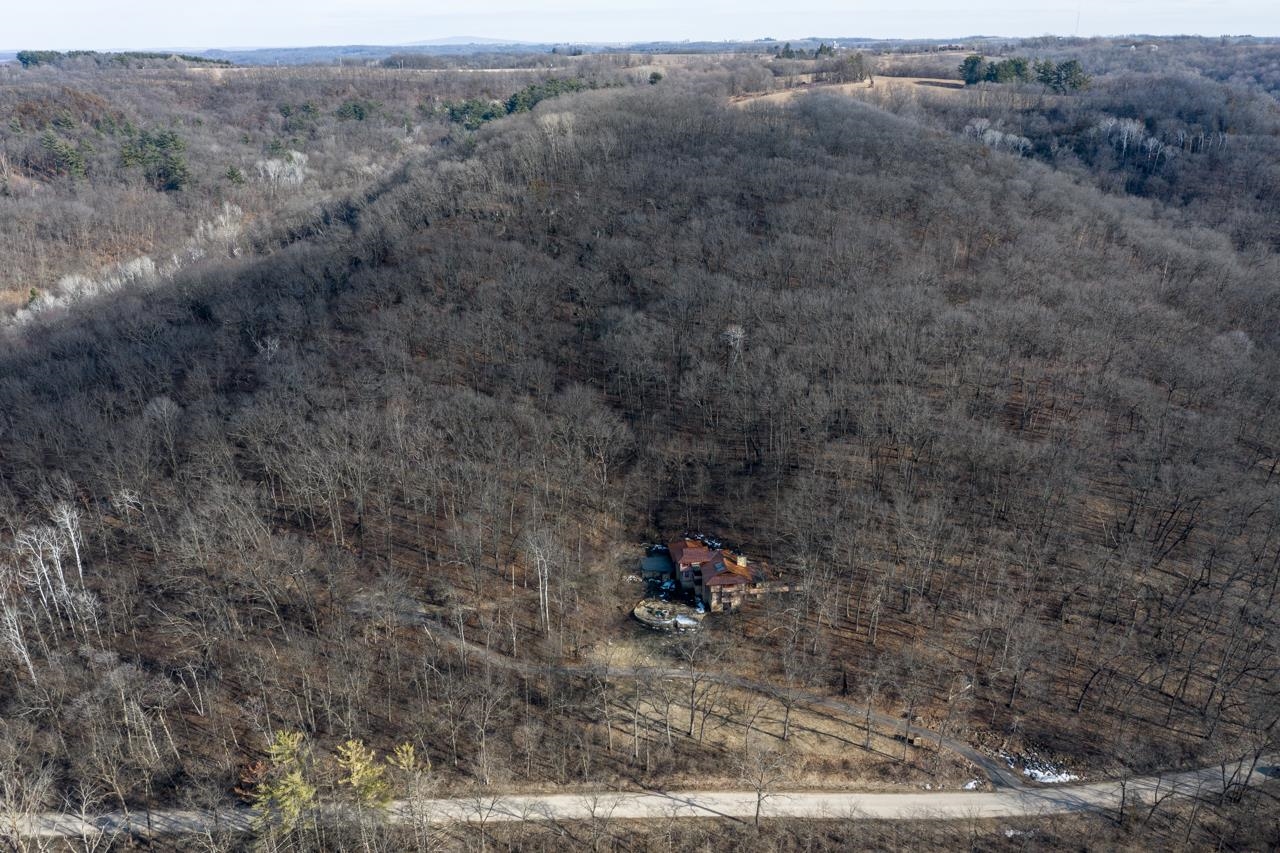 Aerial view of a home amid extensive leafless woodland, with a road in the foreground.